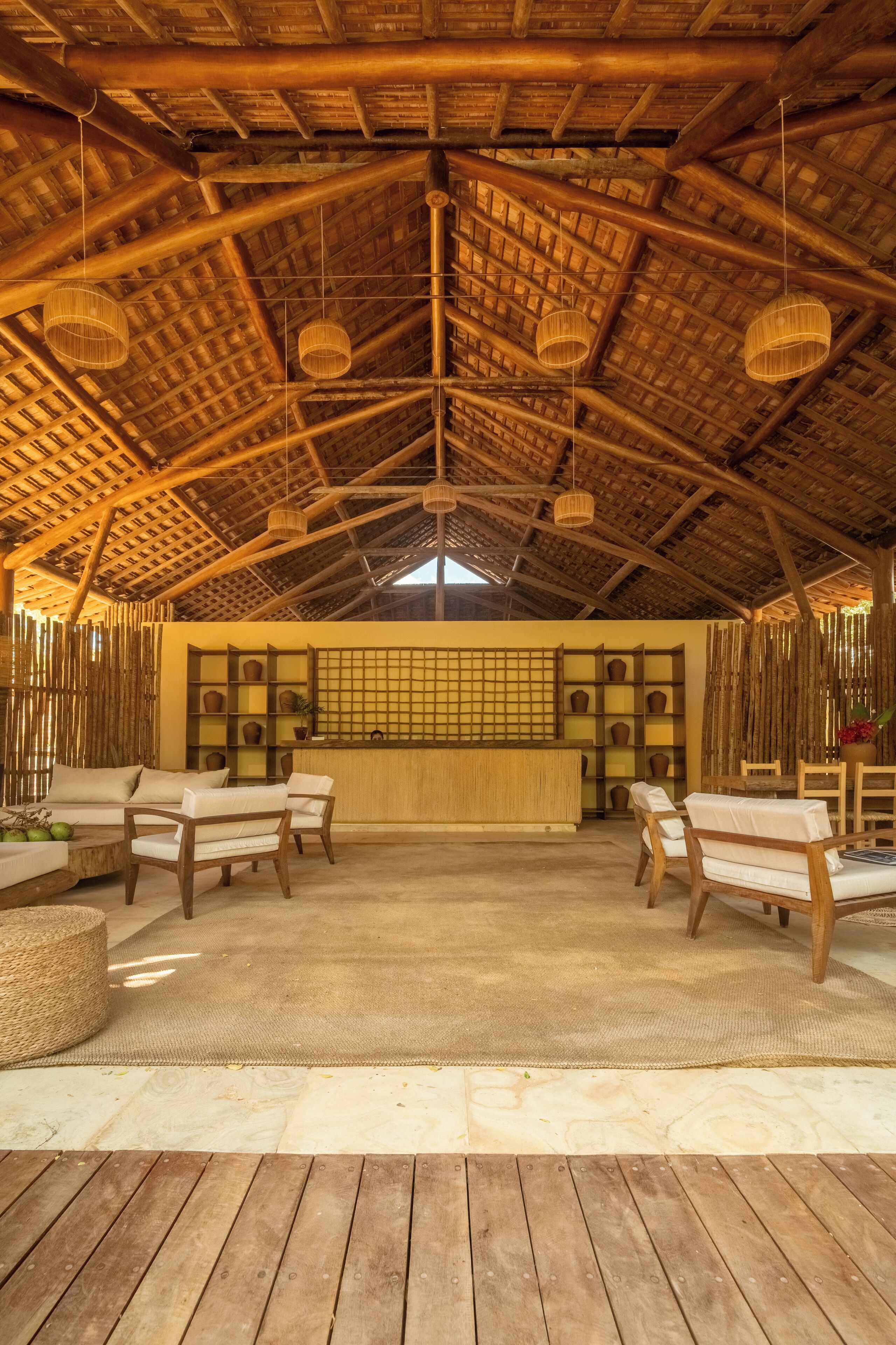 An indoor space with a high wooden ceiling, woven ceiling lamps, and a reception desk with shelves.