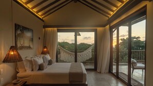 A bedroom with a large bed, two bedside lamps, a hammock, and a view of the outdoors. - Villa Tapi (Jericoacoara)