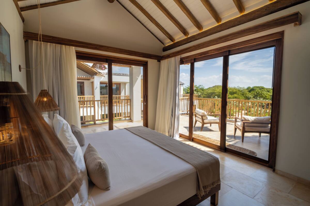 Un dormitorio con una cama grande, un balcón con barandilla de madera y vistas a zonas verdes.