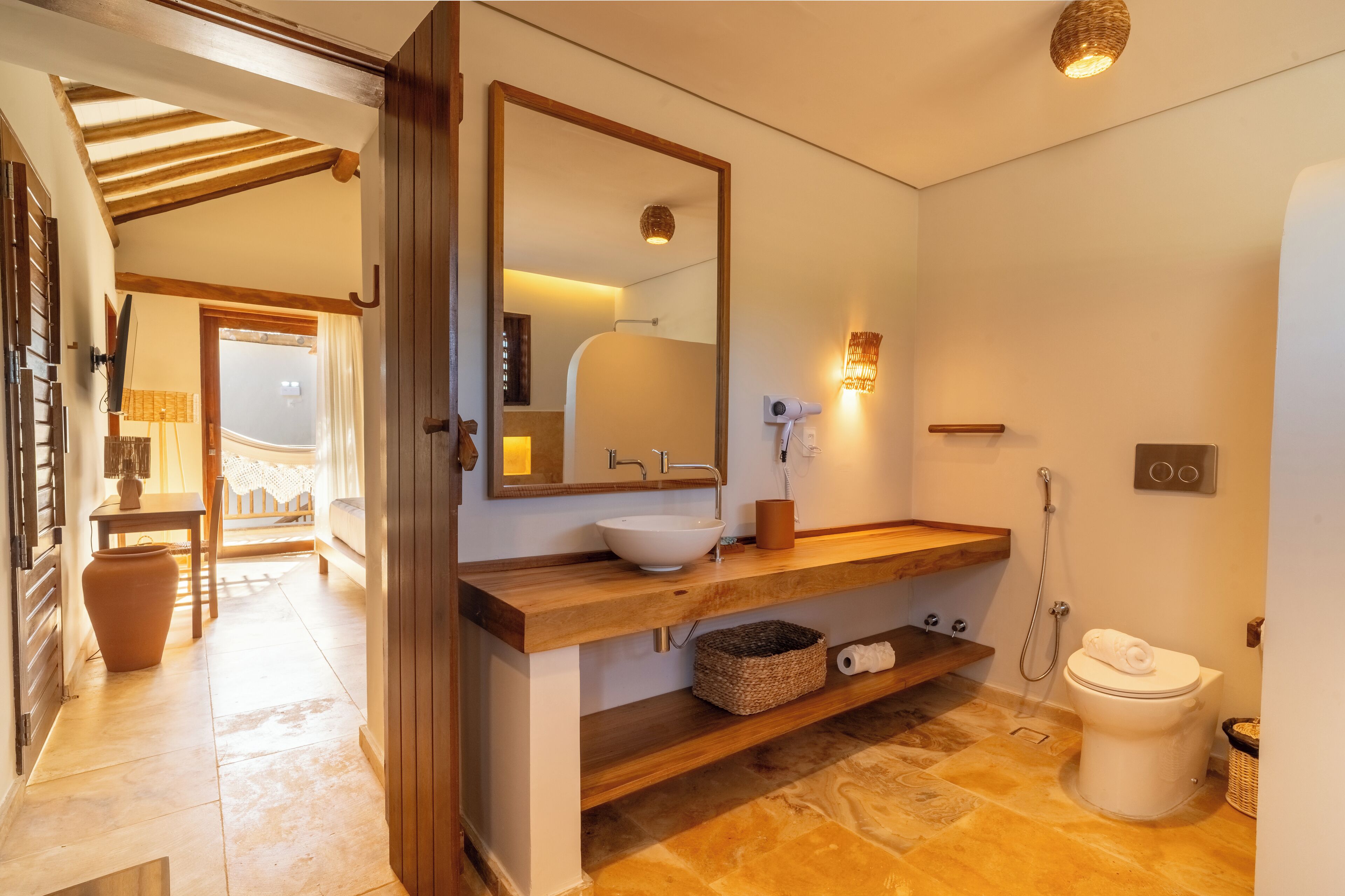 A bathroom with a wooden vanity, a large mirror, a white sink, a towel on the toilet, and a shower area.