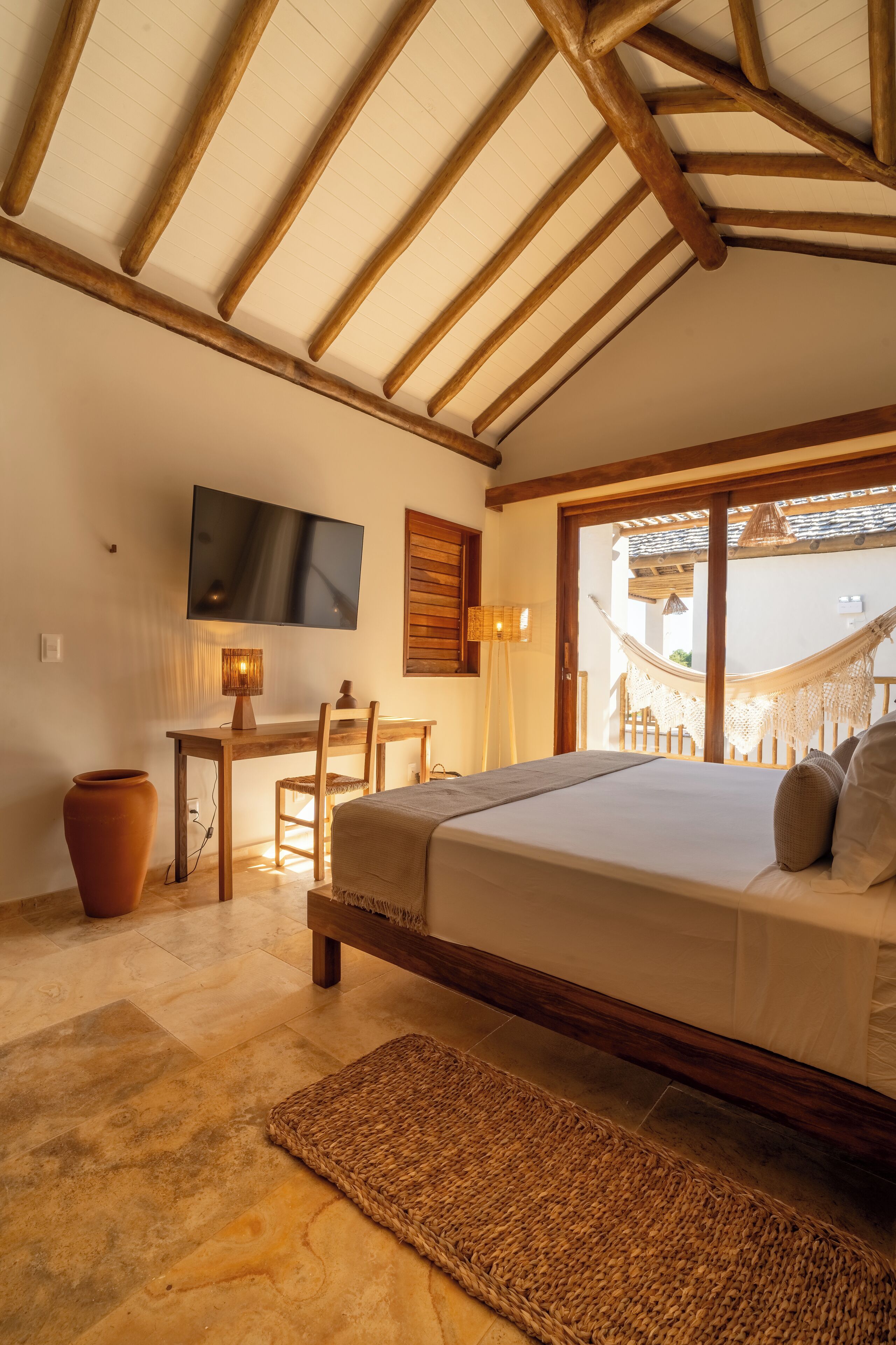 Um quarto com cama, escrivaninha, televisão e rede.