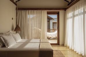 Ein Schlafzimmer mit einem Bett, einer Hängeleuchte und Blick auf einen Balkon mit einer Hängematte.