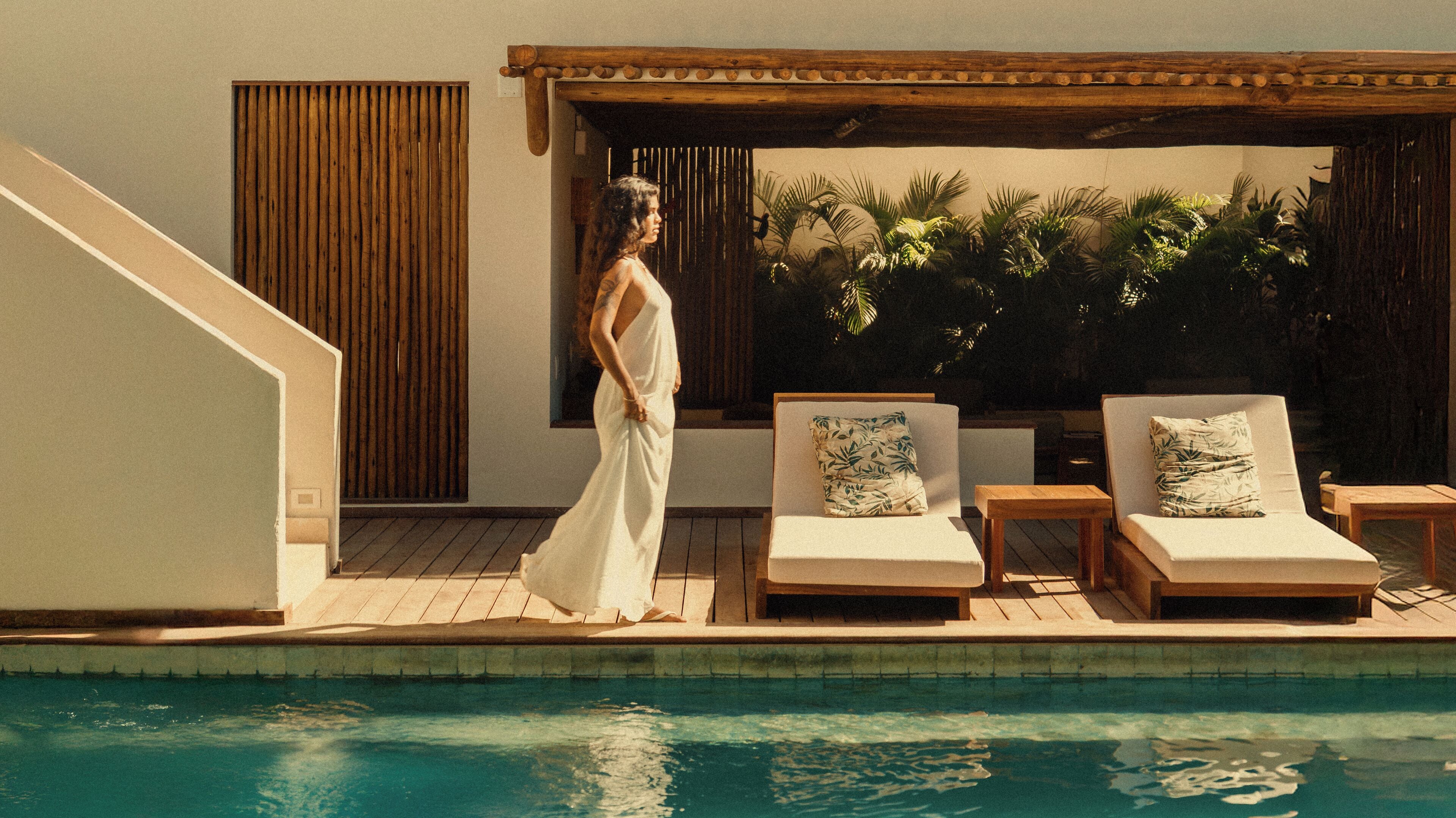 A poolside area with lounge chairs, a wooden pergola, and a view of palm trees.