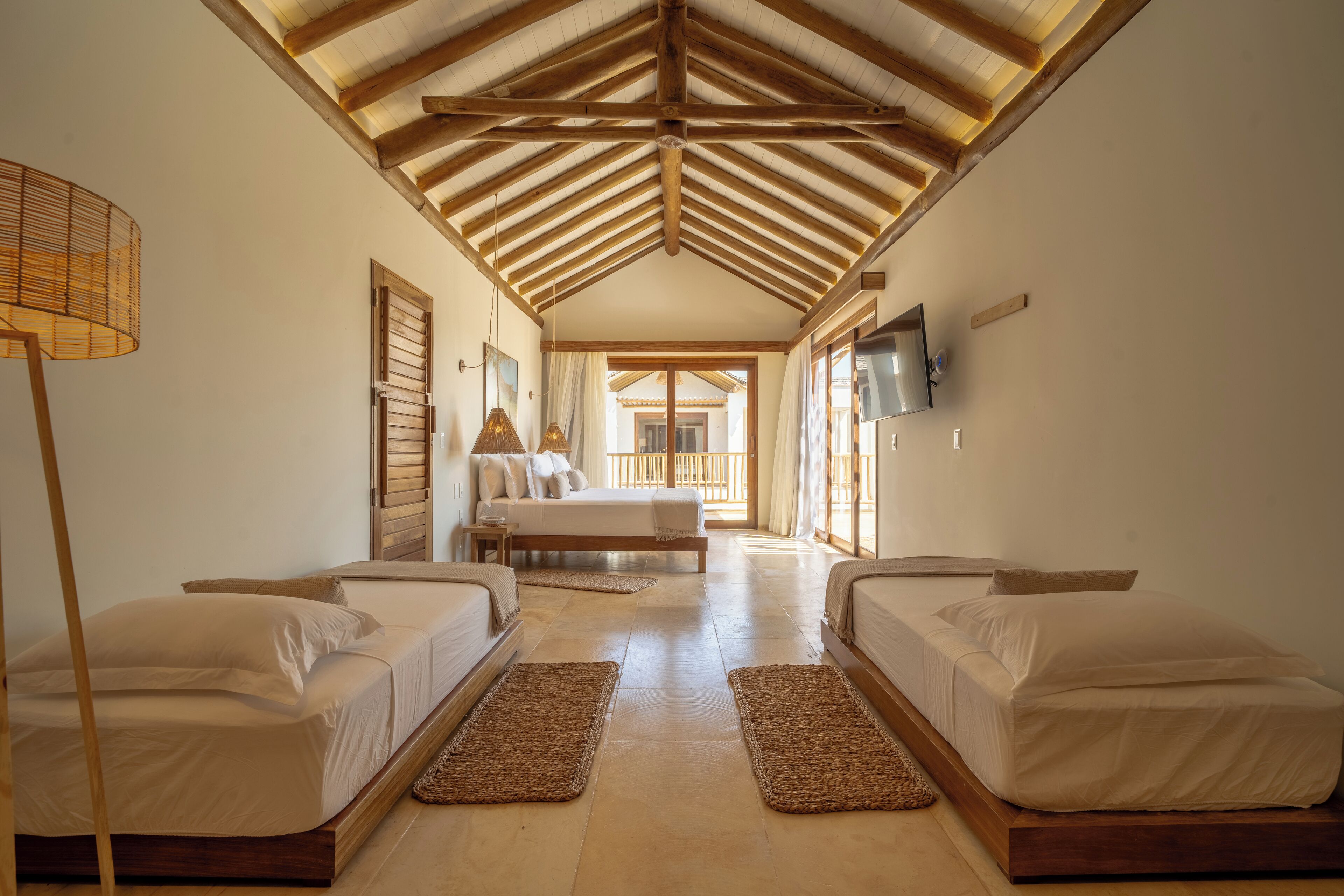 A hotel room with two beds, a wooden ceiling, a TV, and a view of the outside.