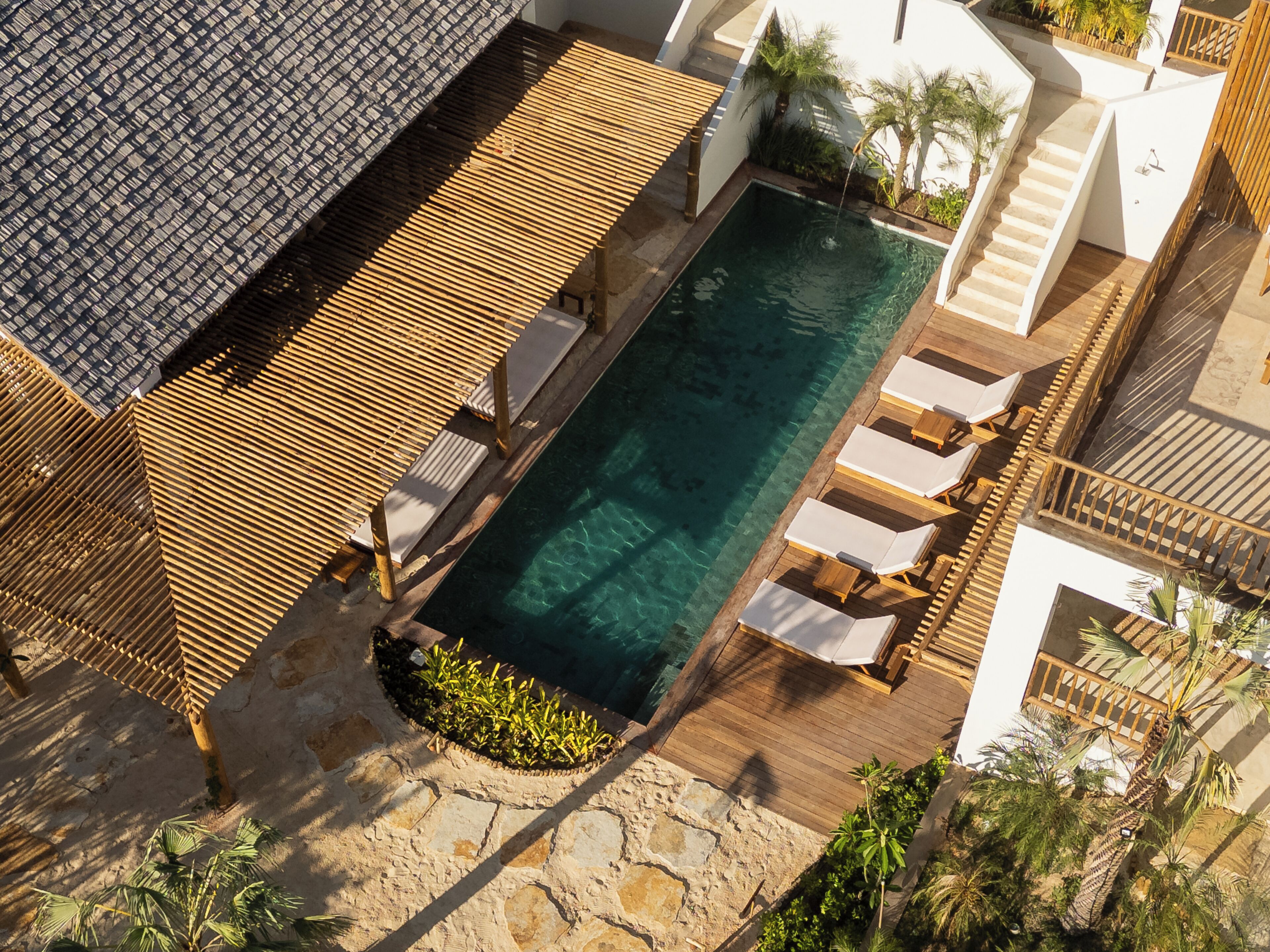 An aerial view of a resort with a rectangular pool surrounded by wooden deck seating and a stone pathway.