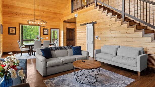A spacious living room with two sofas, a coffee table, and a staircase. - Gettin' By Cozy 2 Bedroom Cabin with Hot Tub & WiFi in Charming Broken Bow (Broken Bow)