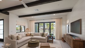 A modern living room with a sectional sofa, ottomans, a coffee table, a TV, and a wooden cabinet. - Fox Point Farms Retreat with Ocean Views - extended stays (Encinitas)