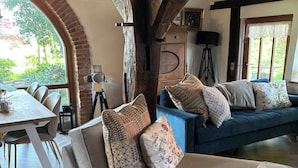 Un salon chaleureux avec un plafond en bois, un canapé agrémenté de coussins à motifs, une table à manger et une vue sur l’extérieur.