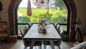 Un espace repas comprenant une grande table, des chaises et une vue à travers une fenêtre en arc de cercle.