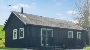 A black wooden house with a sloped roof, two visible windows, and a small porch with a railing.