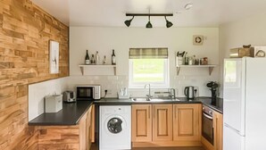 A compact kitchen with wooden cabinetry, a washing machine, a microwave, and a refrigerator.