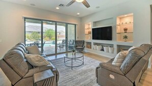 A modern living room with leather sofas, a glass coffee table, and a ceiling fan. - The Desert Jewel in Lucero w/ Private Pool, Jacuzzi, Pool Table! (Goodyear)