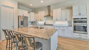 A modern kitchen with white cabinets, a granite countertop, stainless steel appliances, and a bar stool seating area. - The Desert Jewel in Lucero w/ Private Pool, Jacuzzi, Pool Table! (Goodyear)