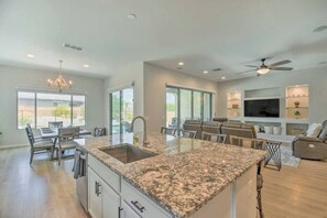 A spacious kitchen with granite countertops, a dining area with a table and chairs, a living room with a sofa and TV, and a ceiling fan. - The Desert Jewel in Lucero w/ Private Pool, Jacuzzi, Pool Table! (Goodyear)