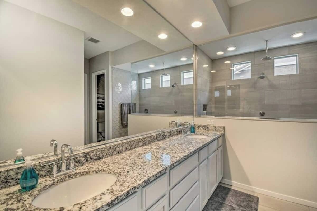 A modern bathroom with a large mirror, granite countertop, and a walk-in shower.