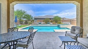An outdoor patio with a pool, seating, and a view of a house in the background. - The Desert Jewel in Lucero w/ Private Pool, Jacuzzi, Pool Table! (Goodyear)