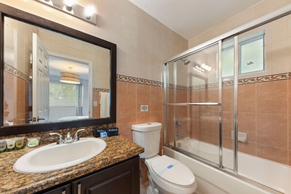 A bathroom with a granite countertop sink, a toilet, and a glass-enclosed shower.