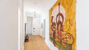 A hallway with wooden flooring, white walls, and a large abstract painting on the right.
