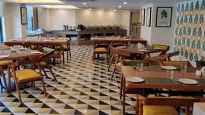 A dining area with checkered flooring, wooden tables, and yellow cushioned chairs. - Spree Hotel Kriday Dehradun (Dehradun)