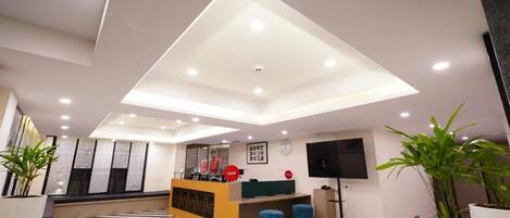 A modern hotel lobby with a reception desk, seating area, and a large flat-screen TV.
