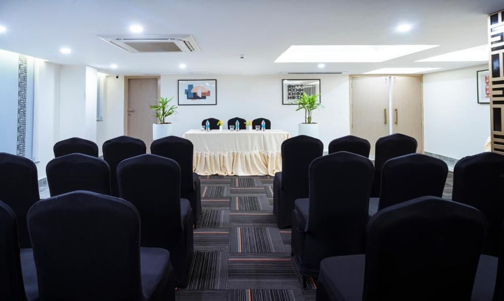 Un salón de conferencias con filas de sillas negras orientadas hacia una mesa con mantel blanco. Hay dos plantas en macetas a cada lado de la mesa.