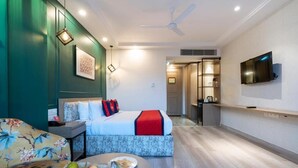 A modern hotel room with a bed, a sofa, a dining table with fruit, a TV, and a ceiling fan. - Spree Hotel Kriday Dehradun (Dehradun)