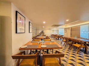 A dining area with multiple tables and chairs, framed artwork on the walls, and a patterned floor. - Spree Hotel Kriday Dehradun (Dehradun)