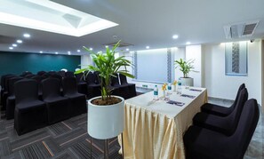 Una sala de conferencias con una larga mesa, sillas negras y plantas en macetas.