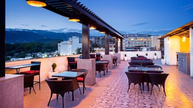 An outdoor terrace with tables and chairs, a pergola, and a view of buildings and mountains. - Spree Hotel Kriday Dehradun (Dehradun)