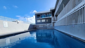 A swimming pool with a white fence, a building with balconies, and a clear blue sky. - 2-bedroom condo in charming Carolina with WiFi, AC. 4 min walk to beach! (Carolina)
