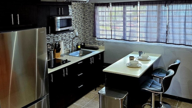 A modern kitchen with a stainless steel refrigerator, a microwave, and a tiled backsplash. - 2-bedroom condo in charming Carolina with WiFi, AC. 4 min walk to beach! (Carolina)