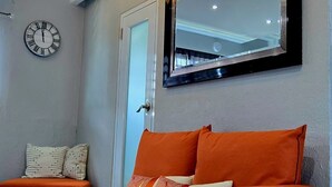 A modern living room with a sofa, a large mirror, and a wall clock. - 2-bedroom condo in charming Carolina with WiFi, AC. 4 min walk to beach! (Carolina)