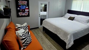 A modern hotel room with a bed, orange sofa, and a wall-mounted artwork. - 2-bedroom condo in charming Carolina with WiFi, AC. 4 min walk to beach! (Carolina)