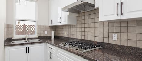Een keuken met witte kastjes, een gasfornuis en een raam met uitzicht op een hek.