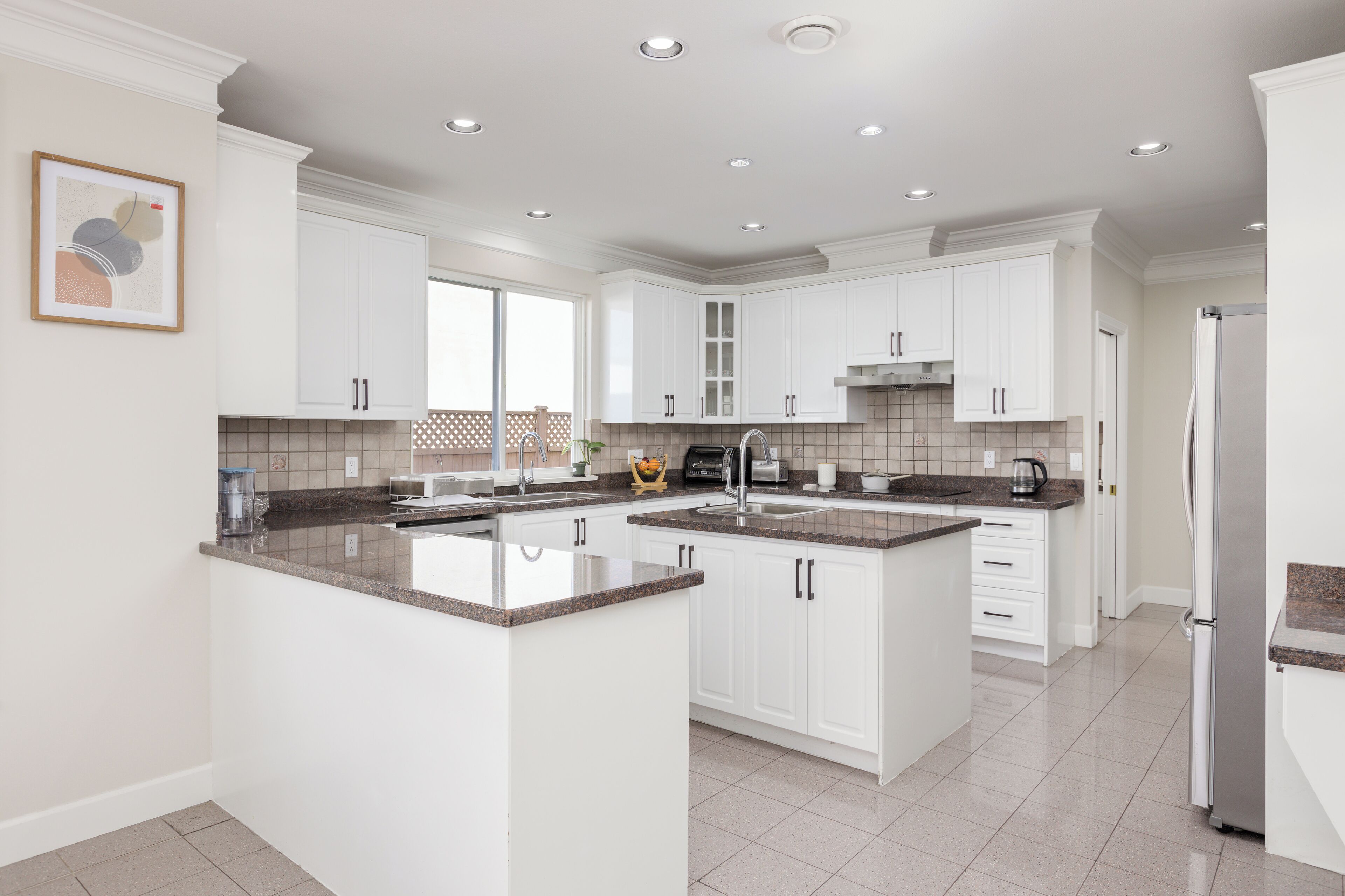 A modern kitchen with white cabinets, granite countertops, and stainless steel appliances.
