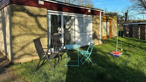 Ein kleines Backsteinhaus mit einer Schiebetür, einer Terrasse mit Tisch und Stühlen sowie einem kleinen Spielbereich mit Ball und Spielzeug.