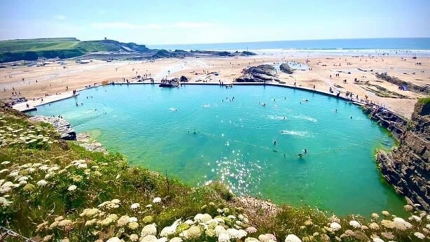 Ein großer, klarer Pool, umgeben von Sandstrand und felsigem Gelände.