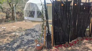 Une structure en forme de dôme géodésique, entourée d’une clôture noire et agrémentée de plantes en pot.