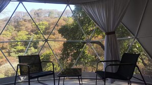 Une pièce dotée d’une grande fenêtre donnant sur un paysage boisé. On y trouve deux chaises et une petite table.