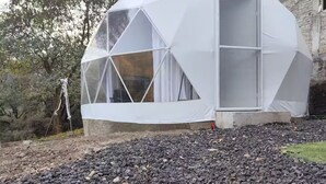 Une structure en forme de dôme géodésique, dotée de grandes fenêtres et d’un sol recouvert de gravier.