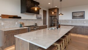 A modern kitchen with a large island, wooden cabinets, and pendant lighting. - Middle Teton 2N | Stunning Views + Private Balcony (Driggs)