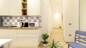Cocina moderna con armarios blancos, microondas, hervidor de agua y una pequeña planta en maceta.