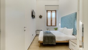 Un dormitorio con cama, ventana, planta y televisor montado en la pared.