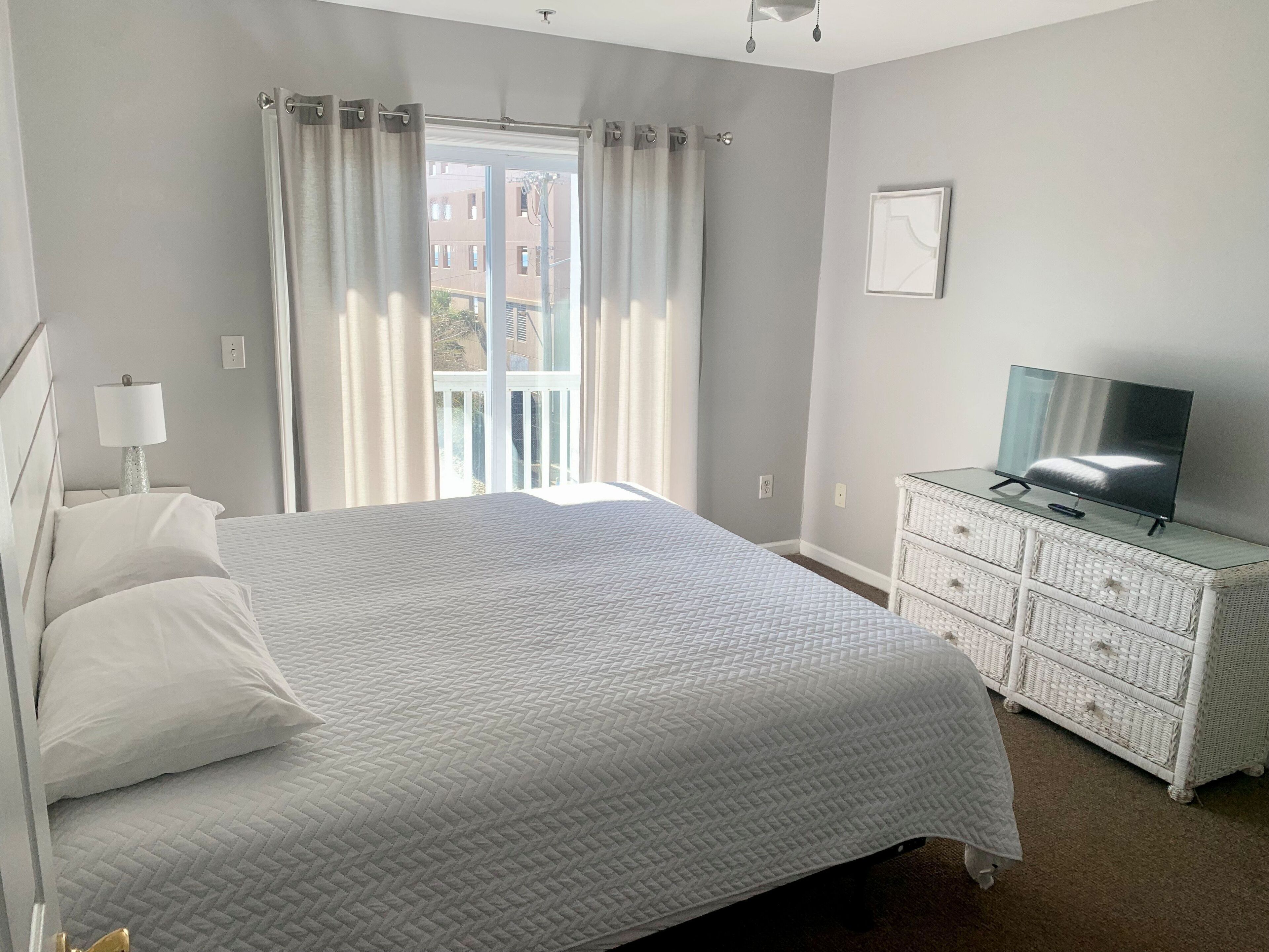 Un dormitorio con una cama grande, un televisor sobre una cómoda y una ventana con cortinas.