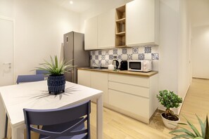 A compact kitchen with white cabinets, a microwave, and a coffee maker. There is a dining table with chairs and a potted plant. - Artis Rooms - Suite Yellow (Cagliari)