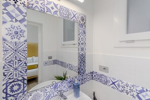 A bathroom with a large mirror, white walls, and blue patterned tiles. - Artis Rooms - Suite Yellow (Cagliari)