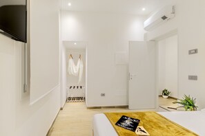 Quarto de hotel moderno com cama, televisão, guarda-roupa e banheiro visível através de uma porta aberta.
