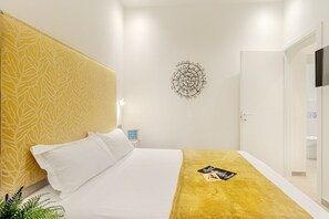 A hotel room with a bed, a bedside table, a wall decoration, and a television mounted on the wall. - Artis Rooms - Suite Yellow (Cagliari)