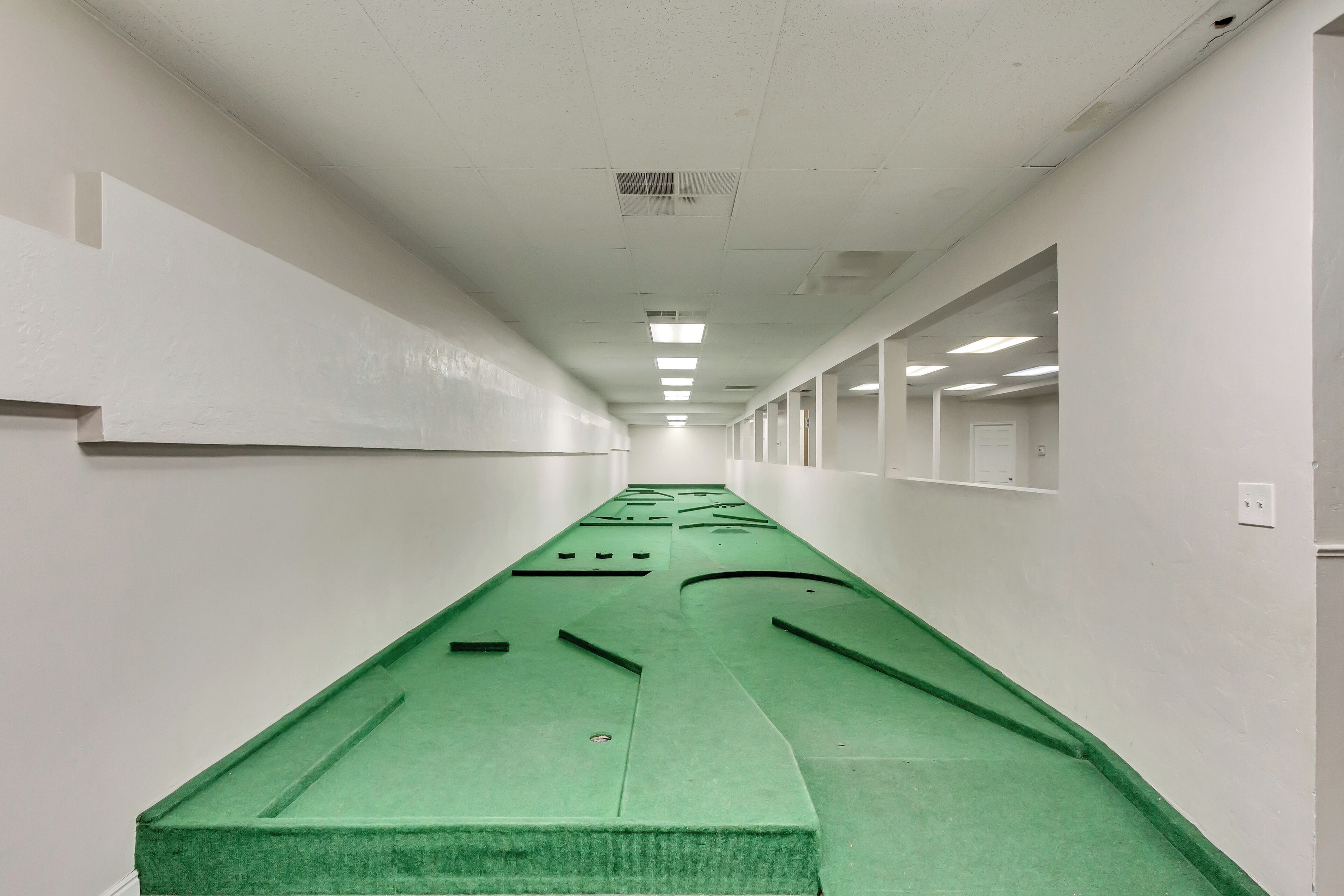 A long, narrow hallway with white walls and a green carpet.