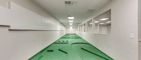 A long, narrow hallway with white walls and a green carpet.